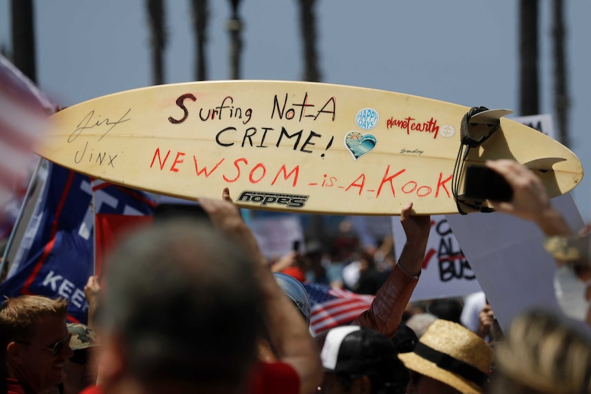 A protestor holds up a surfboard which has 'surfing is not a crime' written on it.