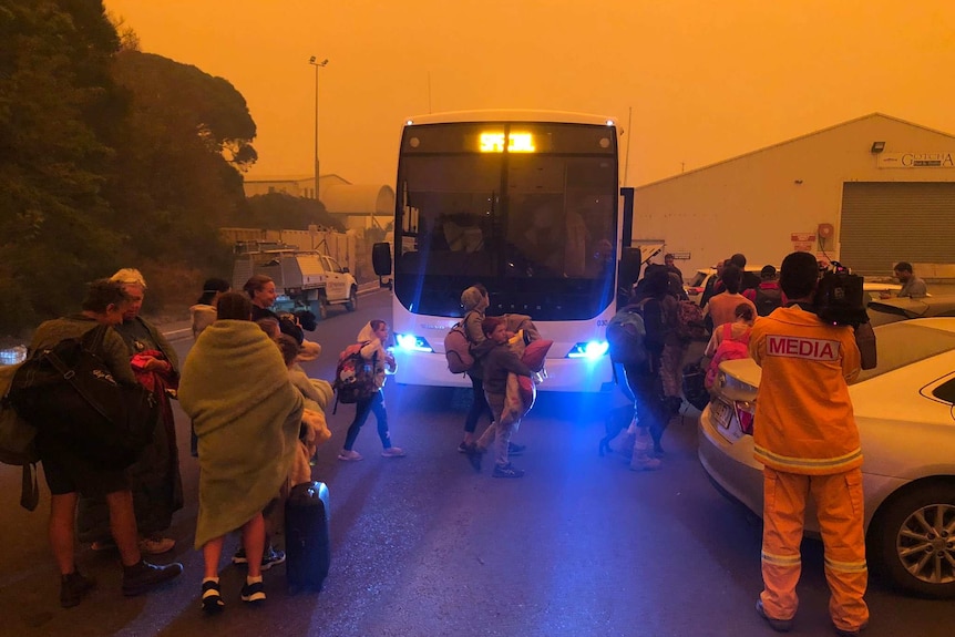 People queue to board a bus under orange skies at Eden.