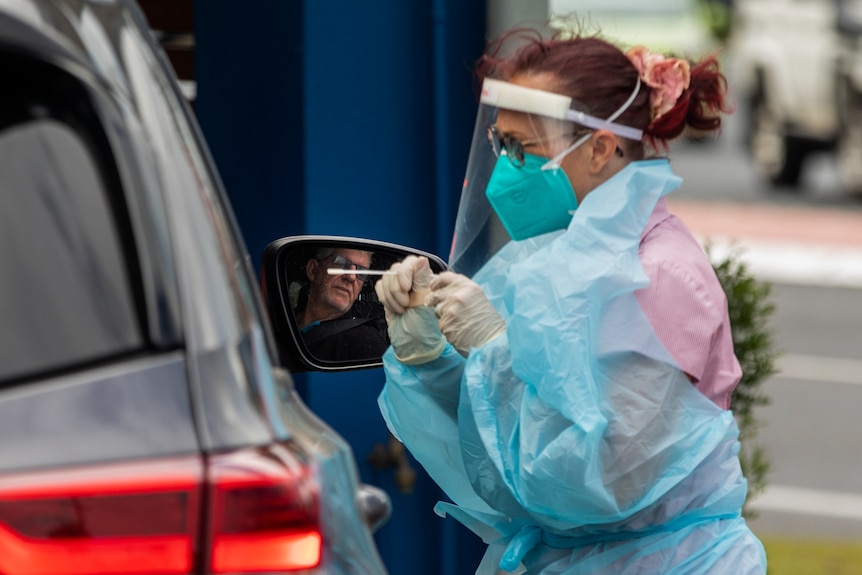 A woman in a mask and plastic coat tests drive in car.