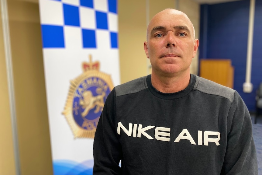 A man in a blue jumper stands in front of a police sign