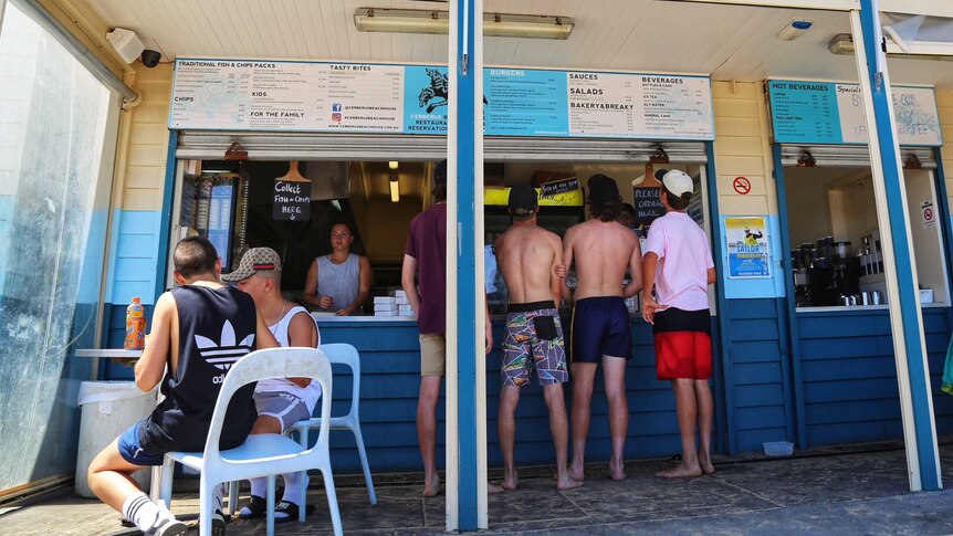 Young men in beach attire at the counter of a kiosk below a sign that says 'Beach House'