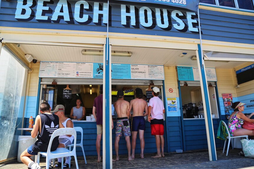 Young men in beach attire at the counter of a kiosk below a sign that says 'Beach House'