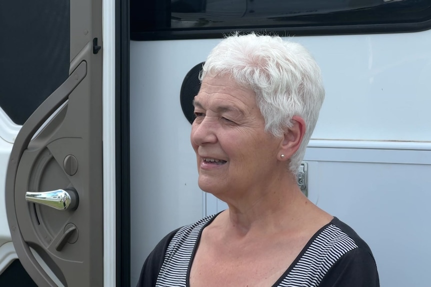A woman with grey hair in front of a caravan