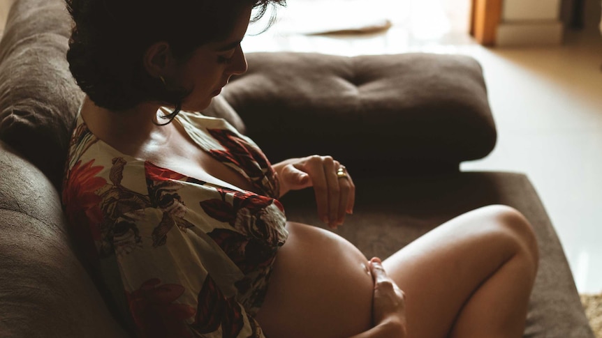 Pregnant woman looks down at her stomach in the shadows for a story on antenatal anxiety
