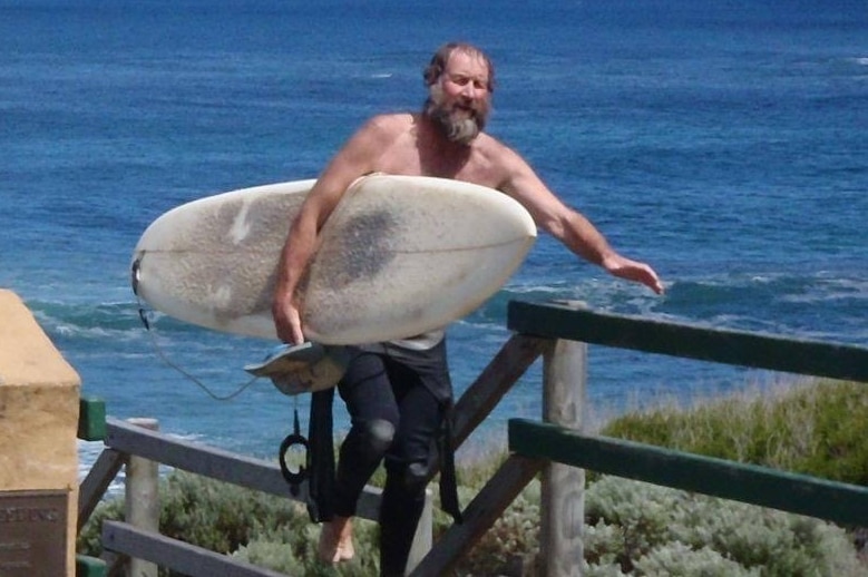 Hardy carries a surfboard up some stairs, from the ocean.