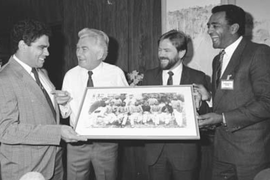 A black and white photo of four men holding a painting.