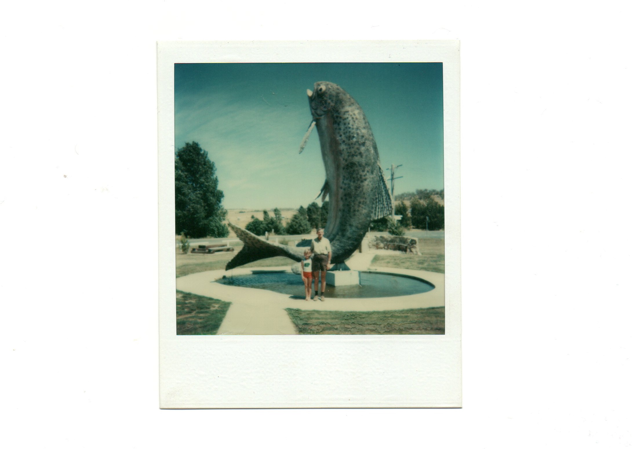 An old photo of two family members posing in front of a statue of a big trout