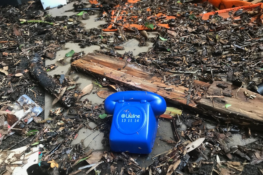 A fake old-fashioned blue telephone is seen surrounded by flood debris on the ground.