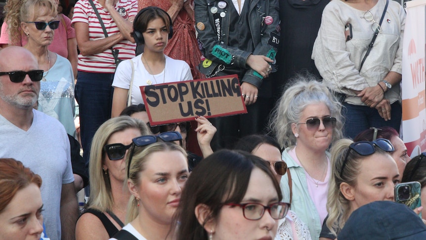 A woman in a crowd holds a sign saying "Stop Killing Us".