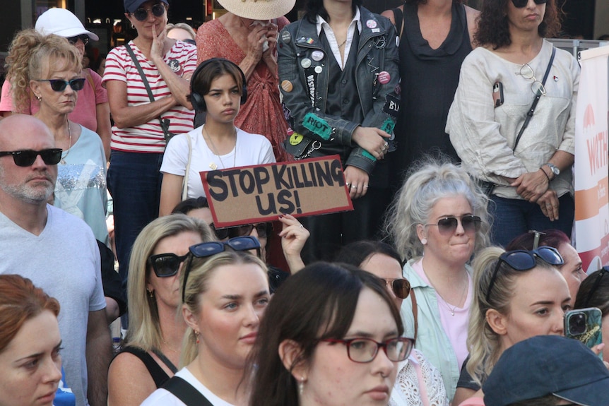 A woman in a crowd holds a sign saying "Stop Killing Us".