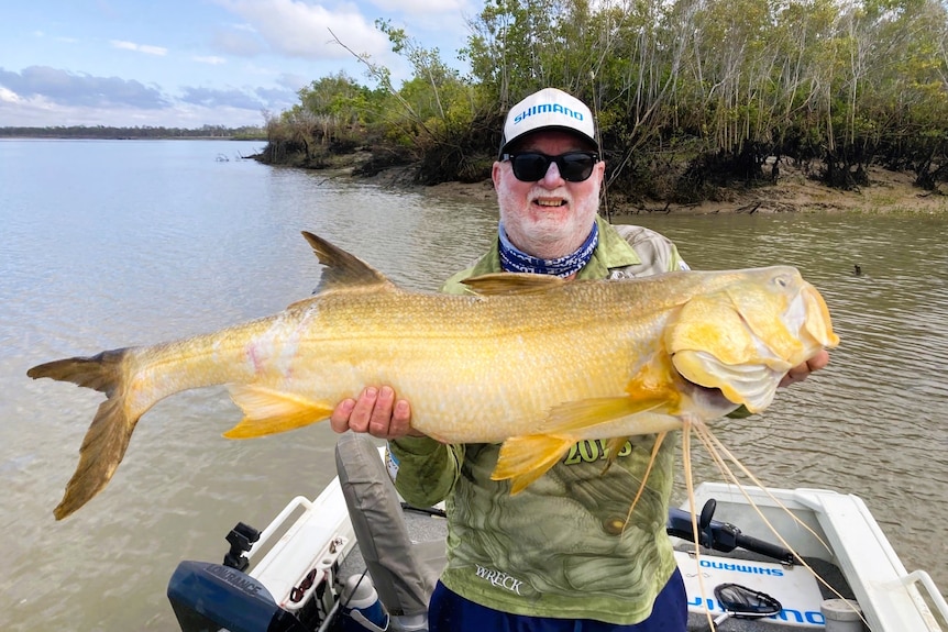 A fisherman standing on a boat holding a large fish.