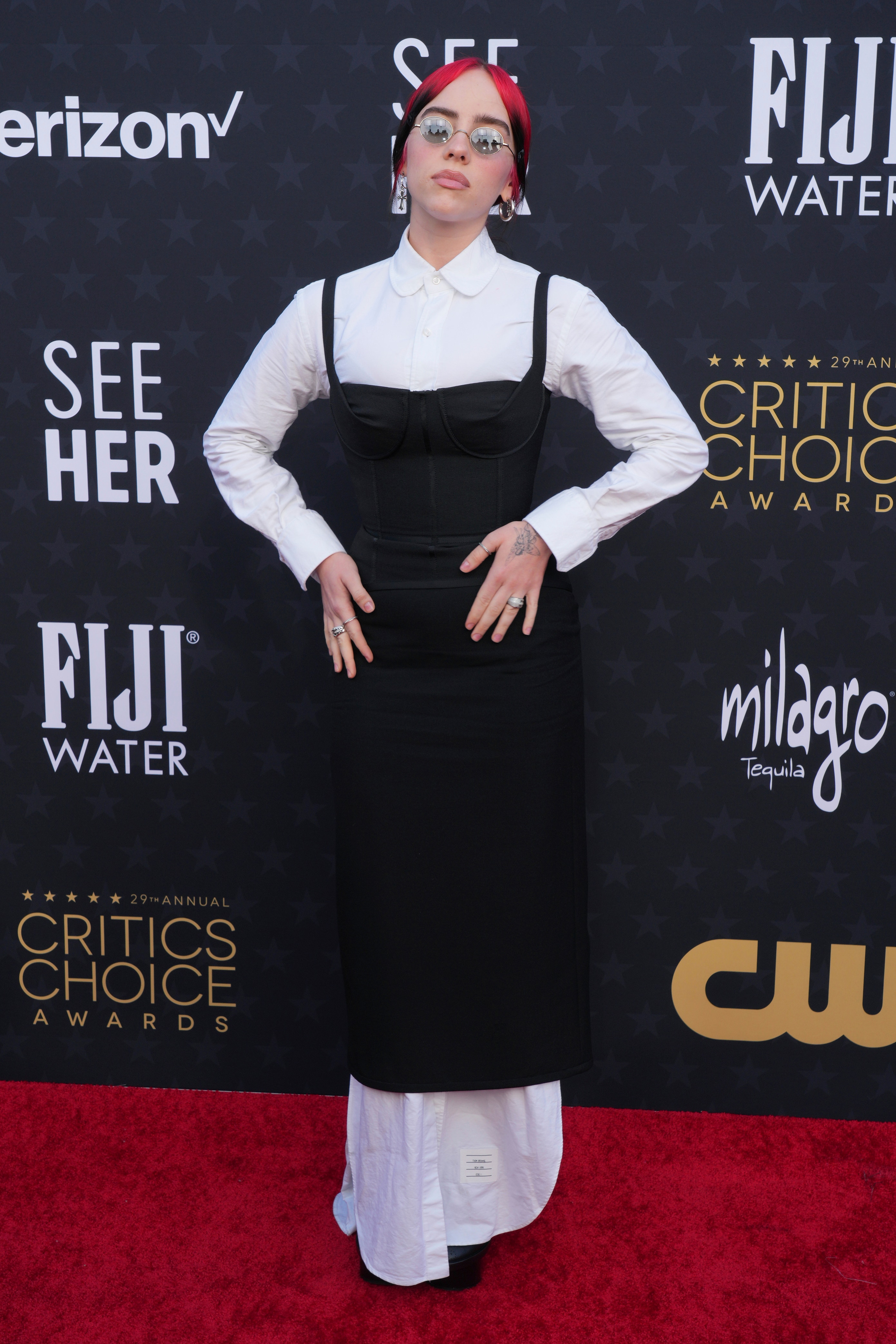 Billie Eilish wearing a black strappy dress over a long-sleeved white button-up shirt with shirt tails handing out the bottom.