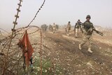 Iraqi Army soldiers walk along a ridge, barbed wire sits in the fore of the image