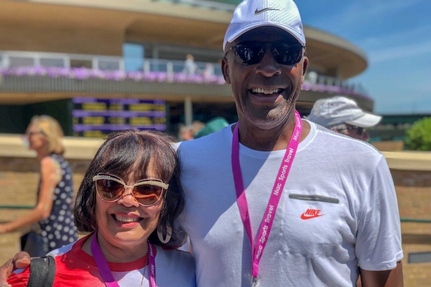 An African American man in sports gear with his arm around a smiling African American woman outside a stadium