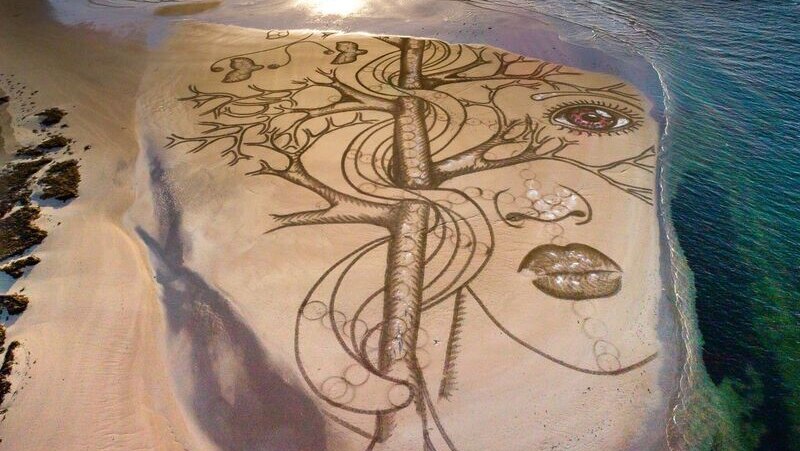 An artwork drawn in the sand on the beach is lapped by the incoming tide