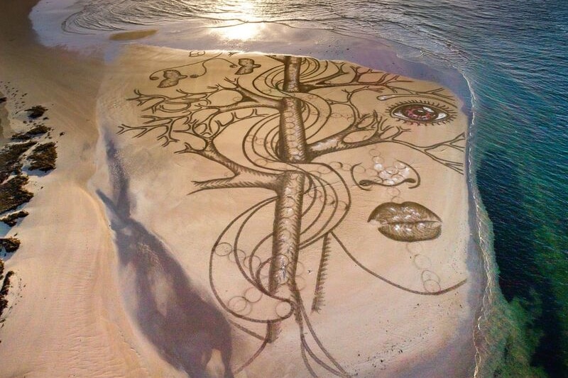 An artwork drawn in the sand on the beach is lapped by the incoming tide