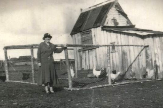 Black and white photo of woman posing next to chicken coop.
