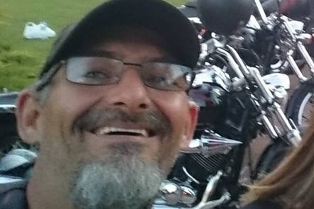 Man with beard smiling at camera with motorbikes  in the backgorund. 