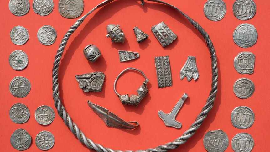 Coins and other medieval jewellery laid out on a red mat.