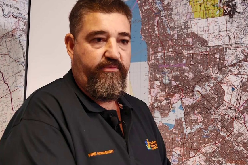 A bearded man sits in front of a map.