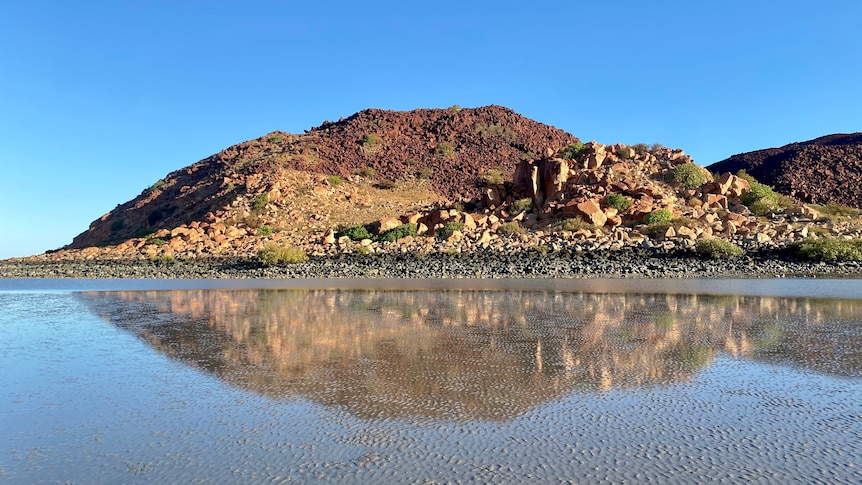 A picture of a rugged hill reflected in still water below