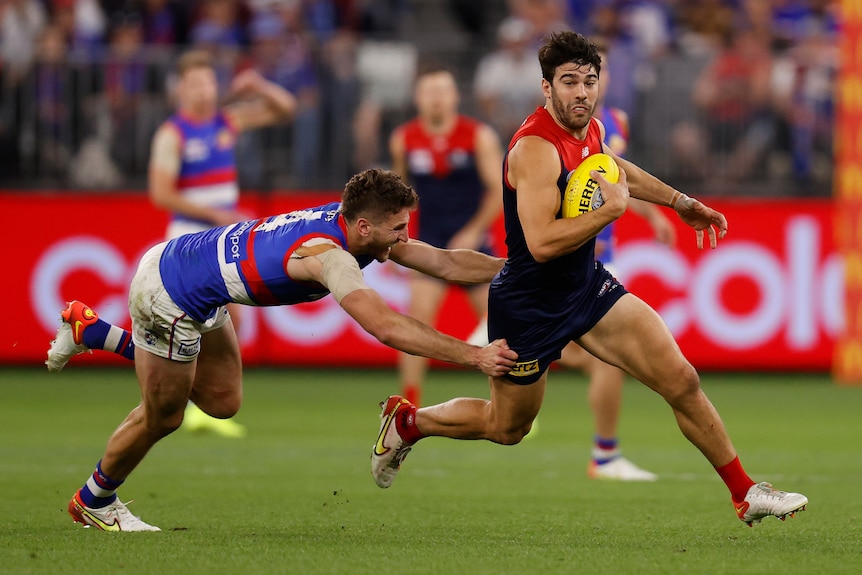 Melbourne's Christian Petracca turns upfield holding the ball as Western Bulldogs' Marcus Bontempelli reaches out to stop him.