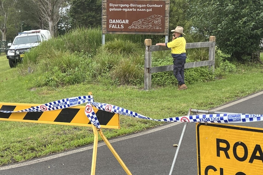police car and police tape close off the entrance to Dangar Falls and a man stands in emergency service clothes