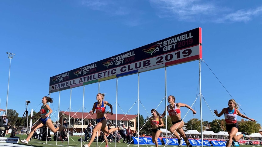 A group of women sprint over the finish line at the Stawell Gift in front of a blue sky.