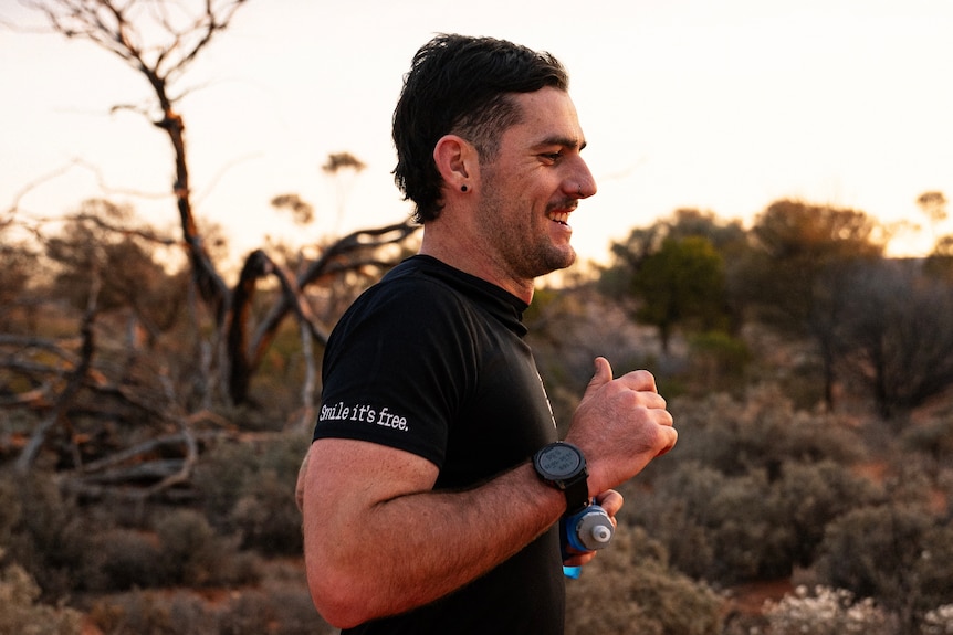 Man smiles whilst running along a bush track. 