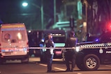Two policemen stand behind police tape and next to police vehicles during counter-terrorism raids.