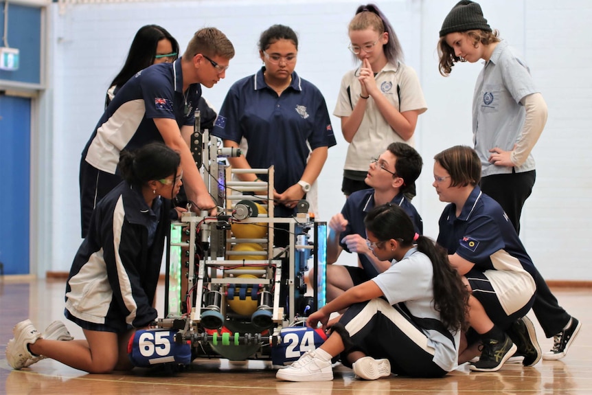 A group of students gather in a gym around some robotic equipment.
