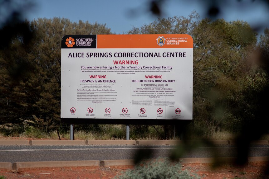 A sign in the bush saying Alice Springs Correctional Centre and outlining various warnings.
