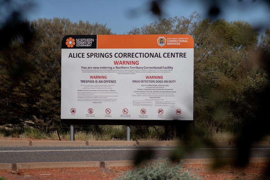 Ein Schild im Busch, das auf die Alice Springs Correctional Facility hinweist und verschiedene Warnungen enthält.