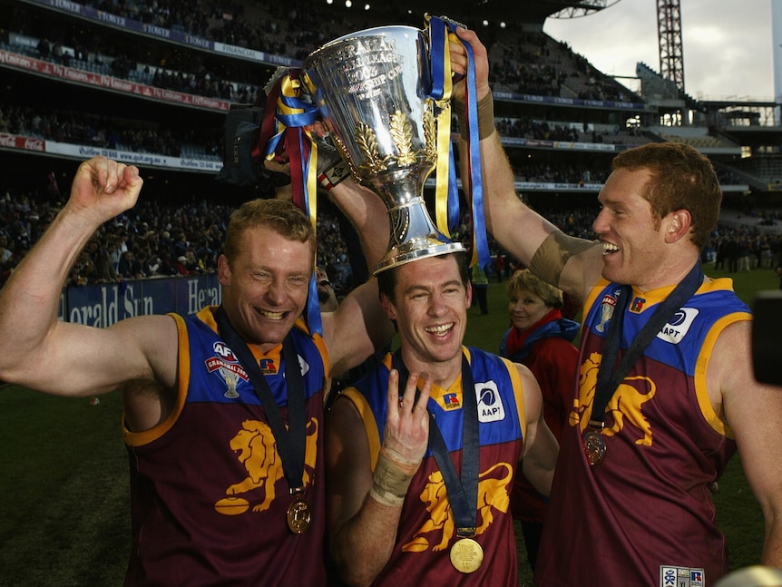 A trio of Brisbane Lions players smile and celebrate with the AFL premiership cup at the MCG.