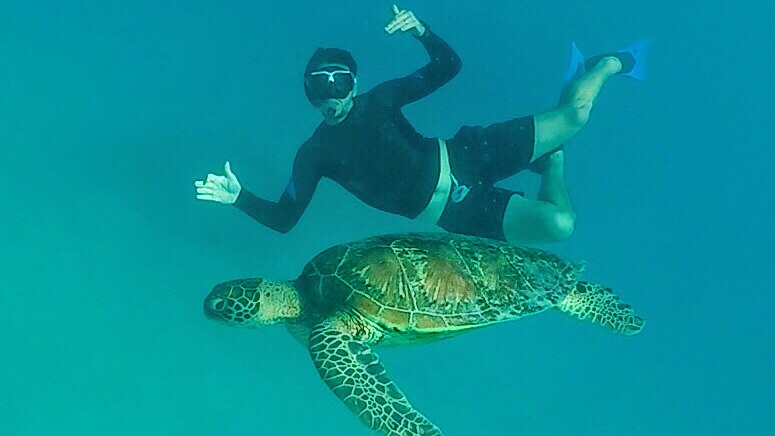 A man swims along side a turtle.