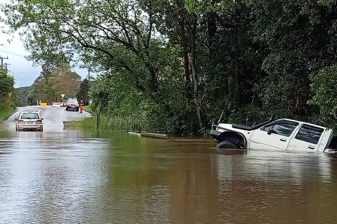 A flooded road, with a vehicle stuck in the brown floodwater.