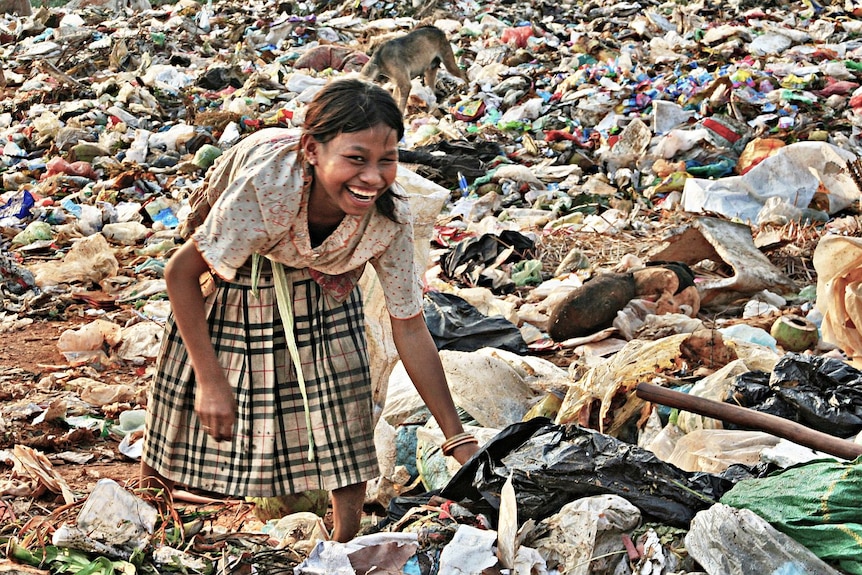 Girl laughs while rummaging for food at a Cambodian rubbish dump