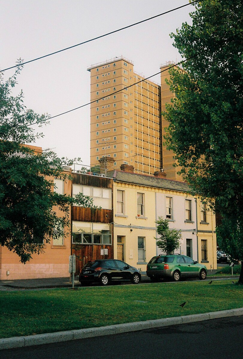 On a cloudy morning, you view a public housing tower looming over two-storey terrace houses in the foreground.