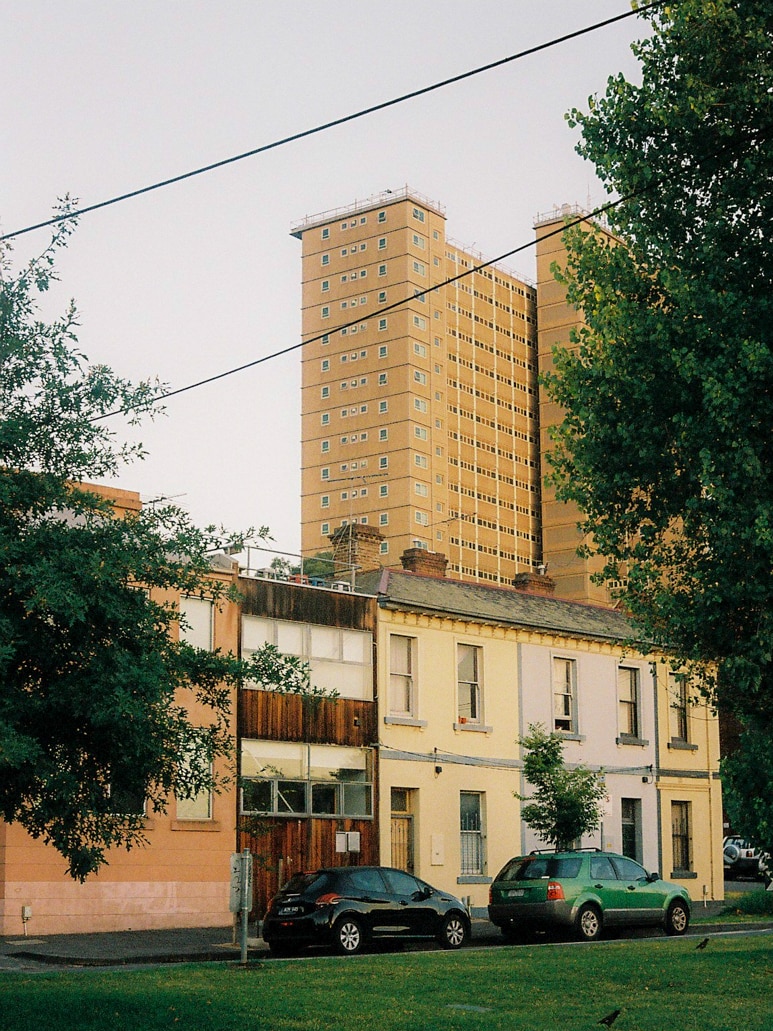 On a cloudy morning, you view a public housing tower looming over two-storey terrace houses in the foreground.