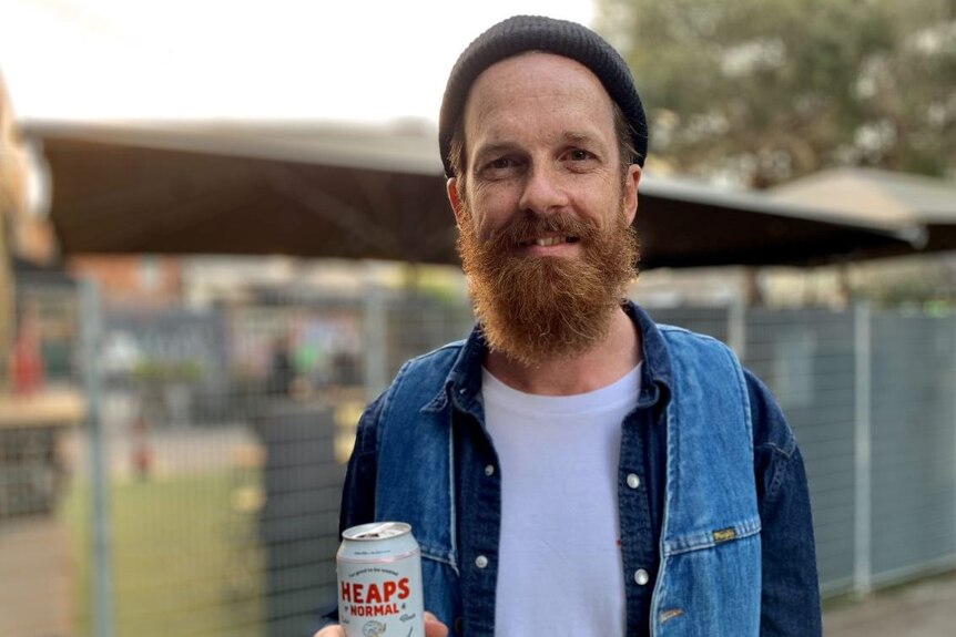 A man in a beanie holds onto a can of non-alcoholic beer.