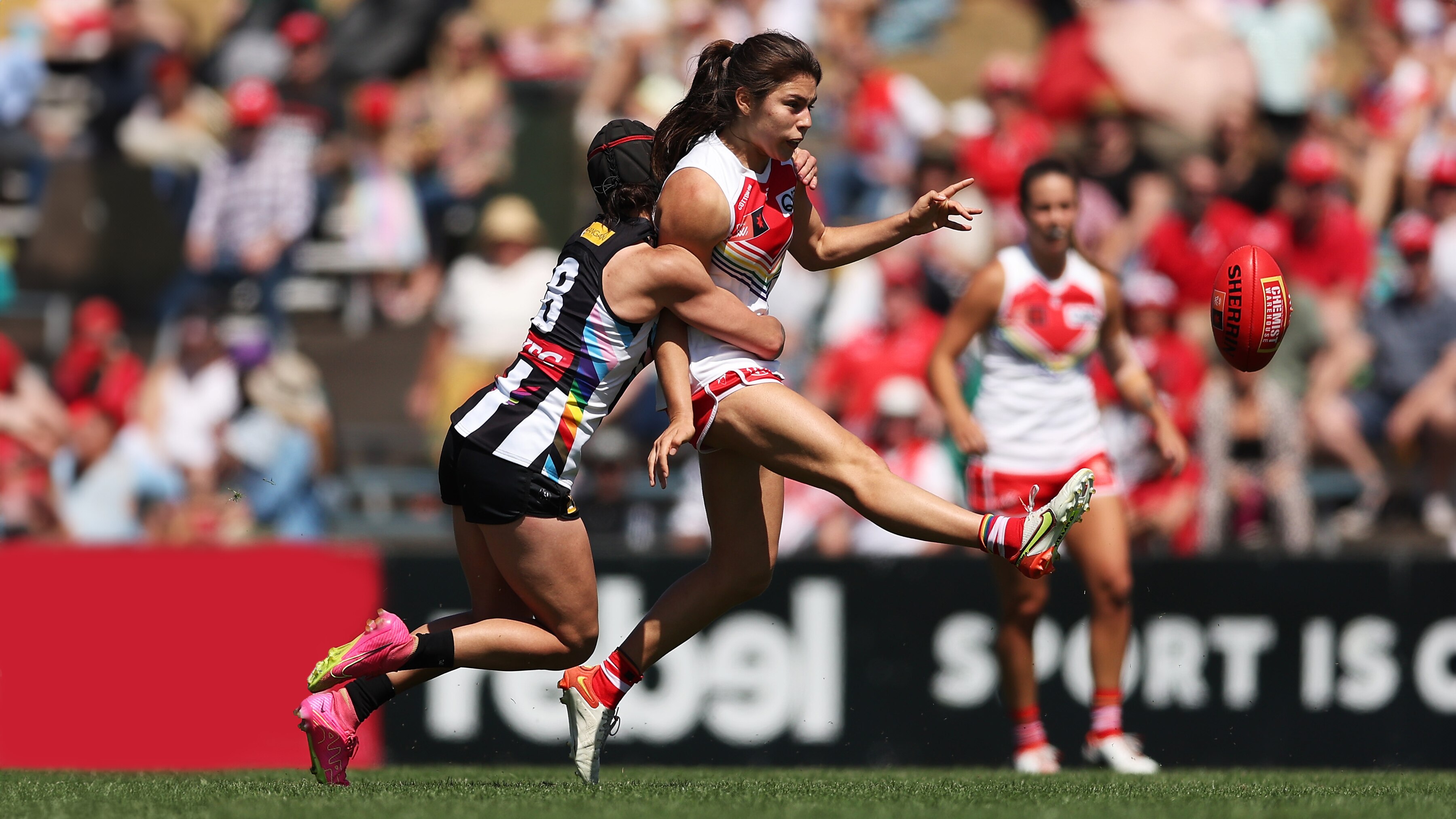 Two AFLW players on the field tackling in mid air on a sunny day