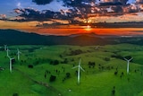 Wide angle aerial view of wind turbines in the foreground with the sun rising in the far distance.
