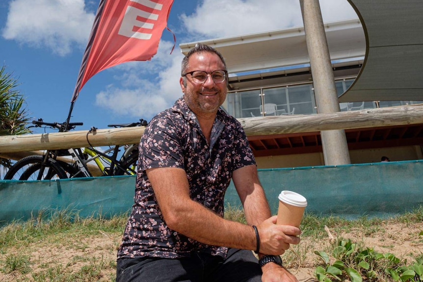 A man holding a compostable coffee cup outside a beach cafe