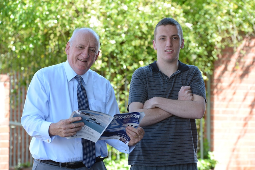 Man in shirt and tie smiles holding an aviation magazine next to man in stripy shirt with crossed arms.