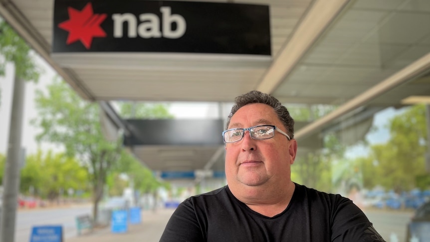 A man stands in front of a NAB bank sign