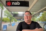 A man stands in front of a NAB bank sign