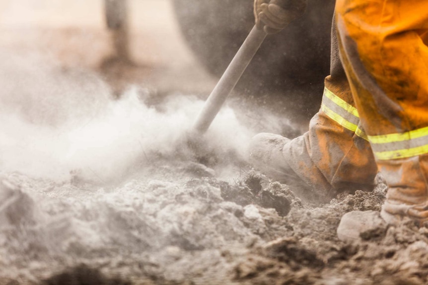 CFA volunteer rakes through the hot earth cooling it down.