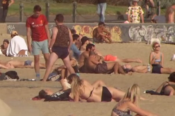 A large number of people sitting on the sand on St Kilda beach.