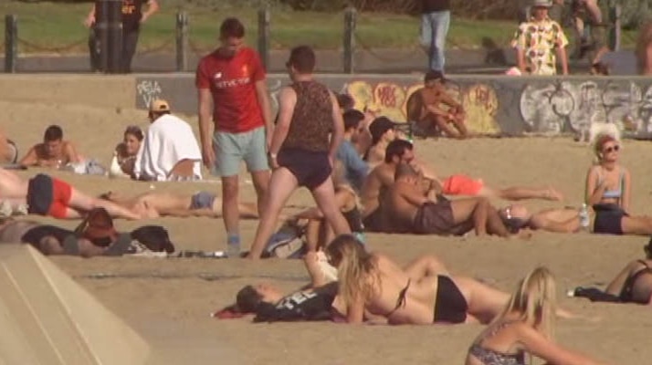 A large number of people sitting on the sand on St Kilda beach.