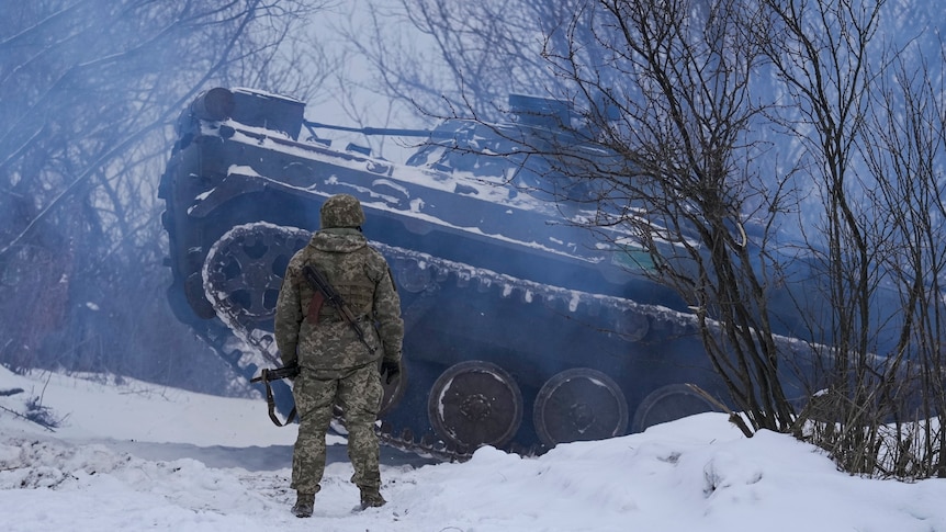 An Ukrainian serviceman stand by as an armored personnel carrier maneuvers in the snow.